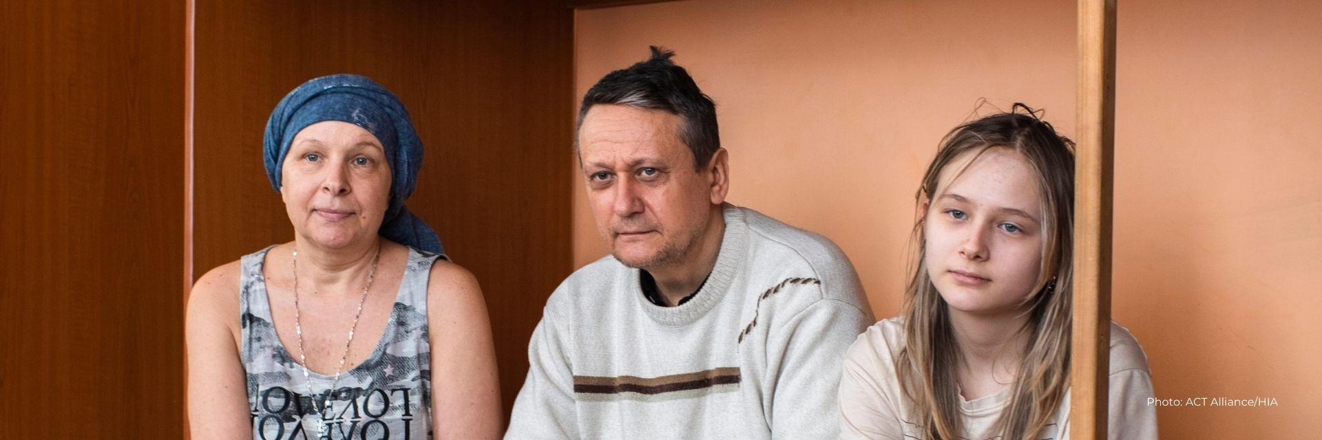 Larysa sits on a bunk bed with her husband and daughter