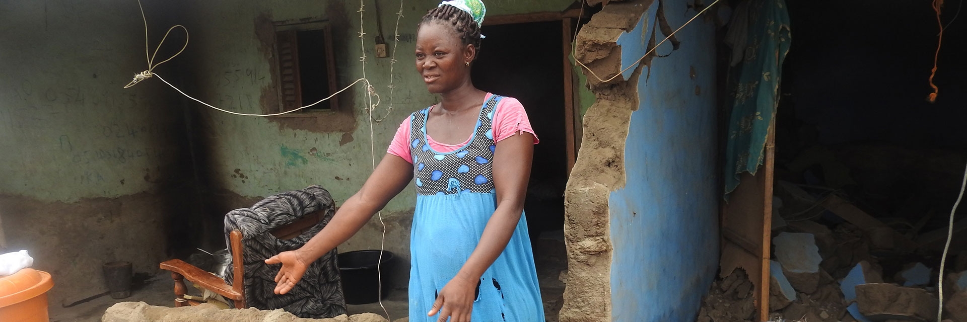 A woman stands in front of her home with outstretched arms