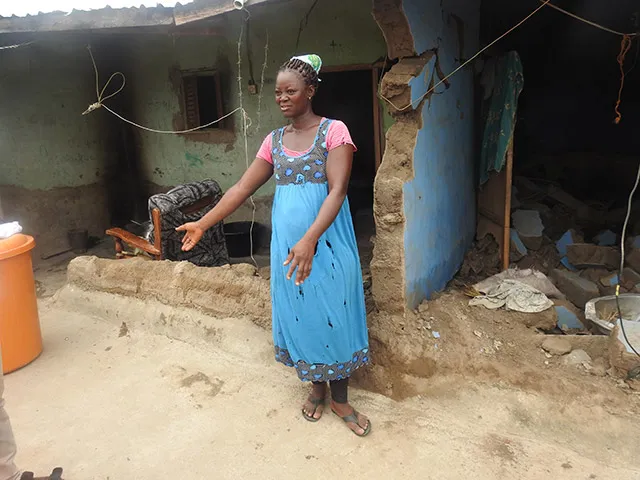 A woman stands in front of her home with outstretched arms